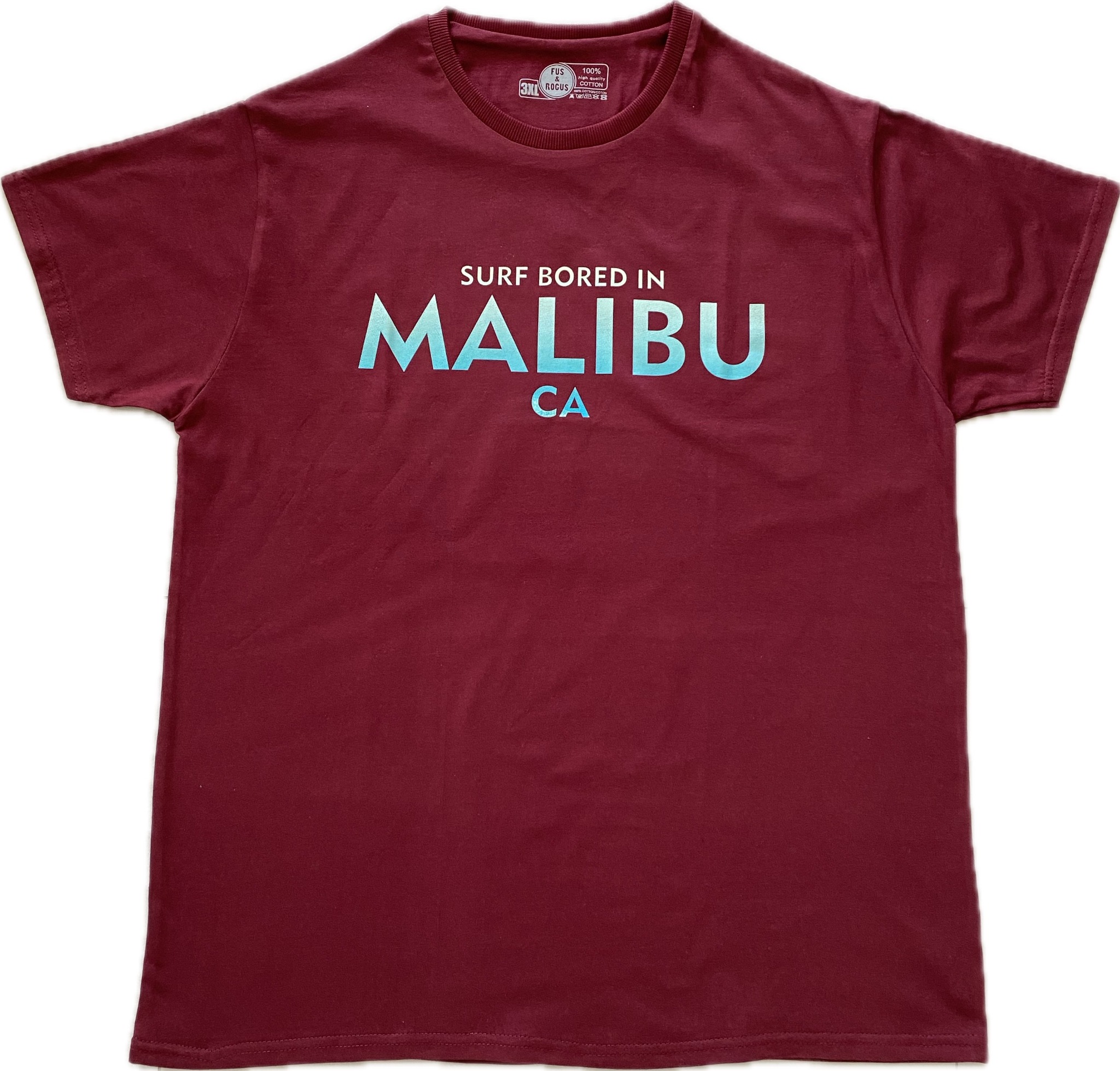 Burgundowa koszulka z krótkim rękawem leżąca na białym tle, z napisem 'Surf Bored In Malibu CA' w jasnoniebieskim kolorze.