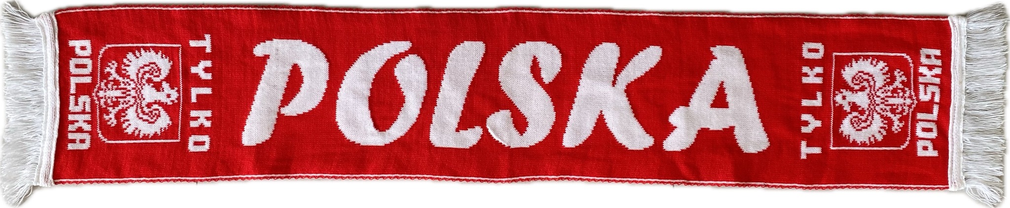 Czerwony szalik z białym napisem 'TYLKO POLSKA' i godłem, zakończony białymi frędzlami, leżący na białym tle.