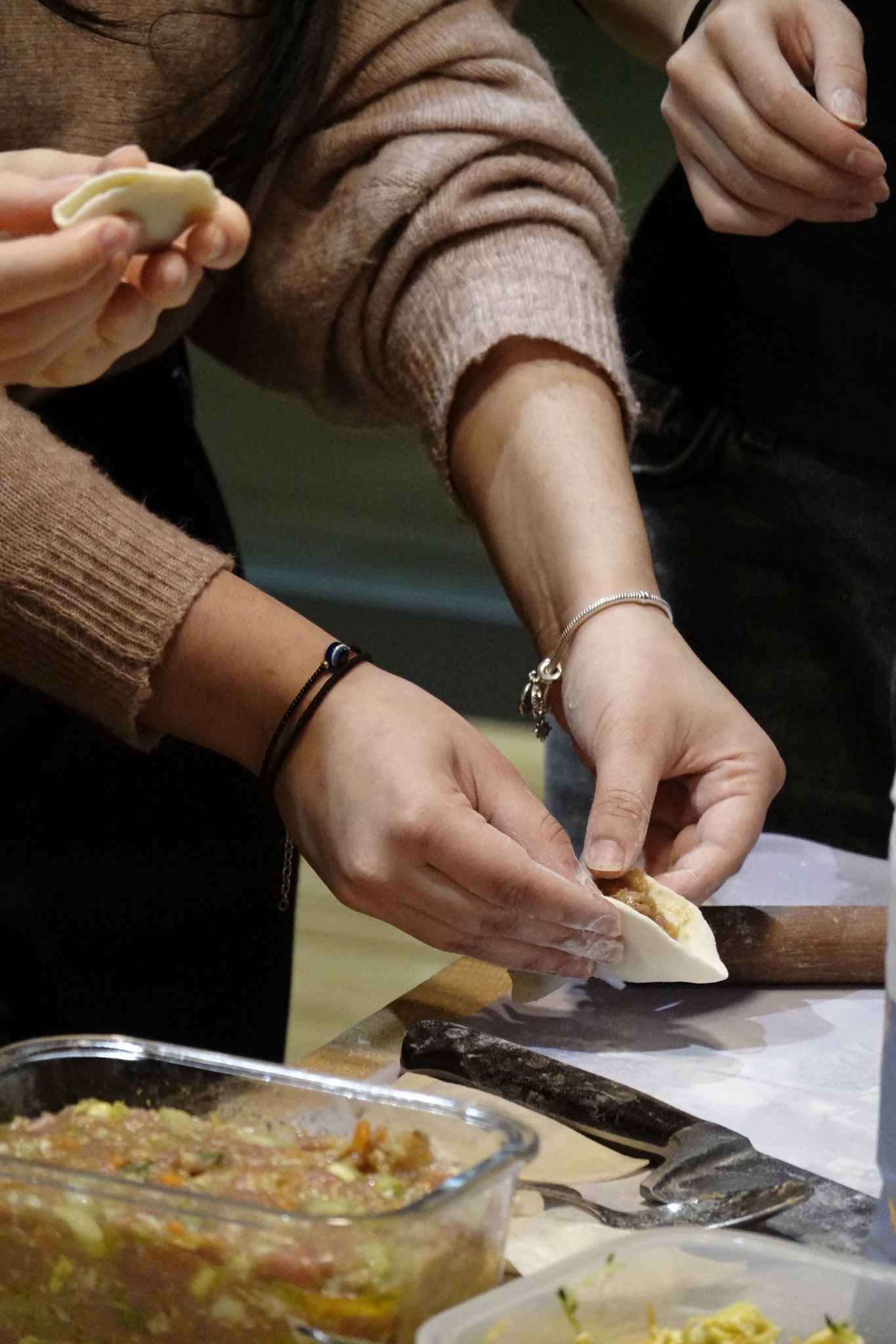Przygotowywanie pierogów na warsztatach kulinarnych w Warszawie: dłonie formują ciasto z farszem, widoczny wałek, nóż i miska z farszem.