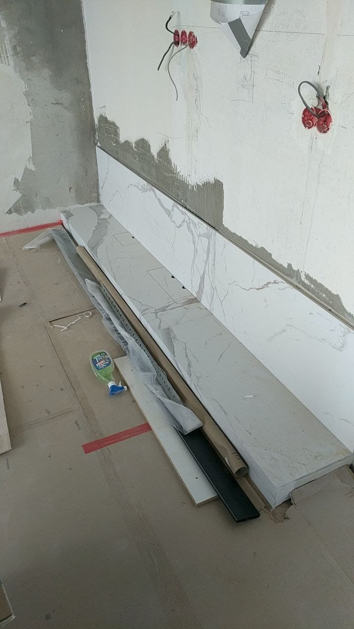 Marmurowe panele ścienne w trakcie montażu, widoczne przewody elektryczne i materiały budowlane na podłodze, sugerujące etap wykończenia wnętrza.