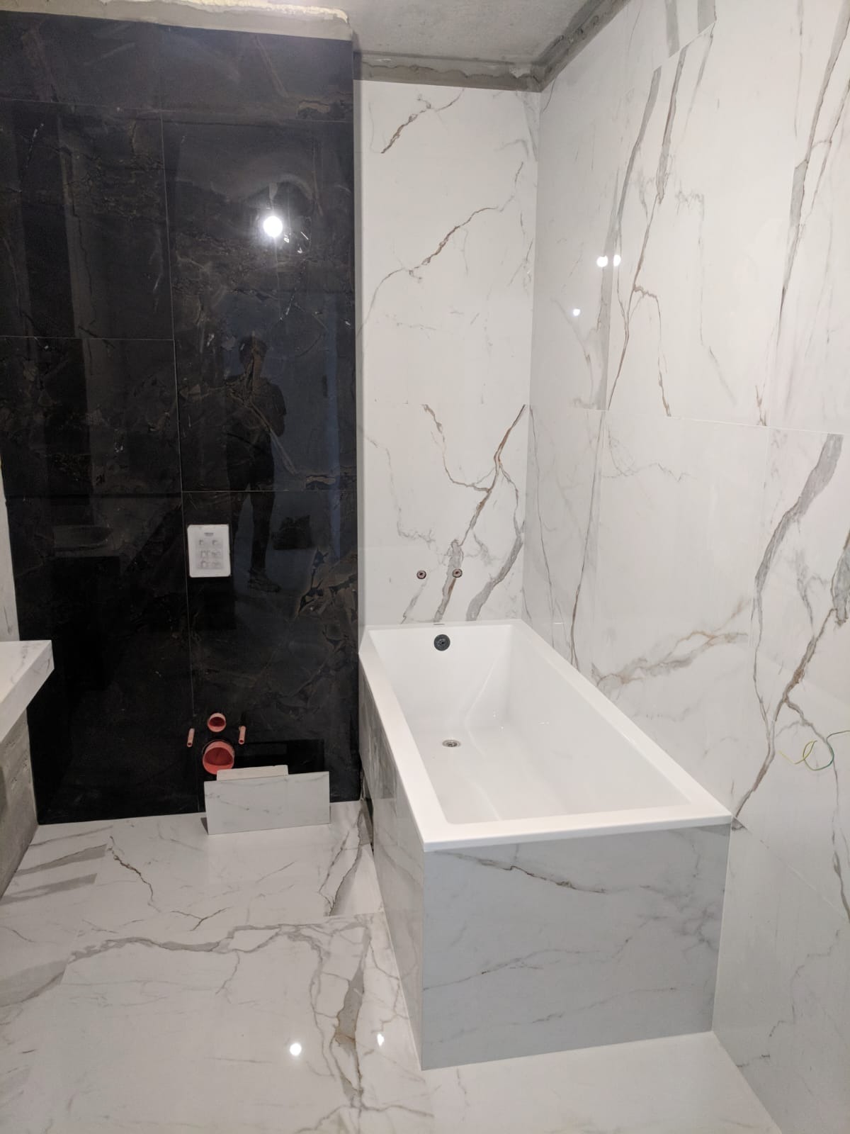 Wykończona łazienka z wanną obudowaną płytkami imitującymi marmur, czarne płytki na ścianie, podłoga również wyłożona płytkami z marmurowym wzorem.