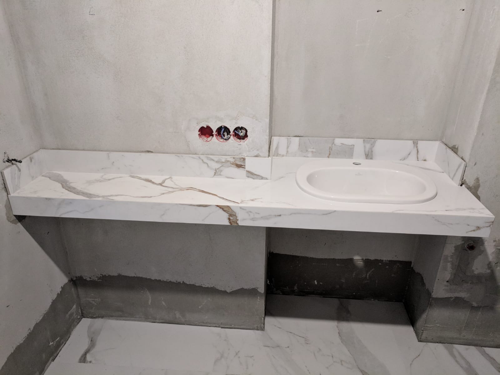 Marmurowy blat z umywalką w łazience w trakcie wykończenia. Widoczne niedoskonałości ścian i podłogi. Ujęcie z bliska na zamontowaną umywalkę.
