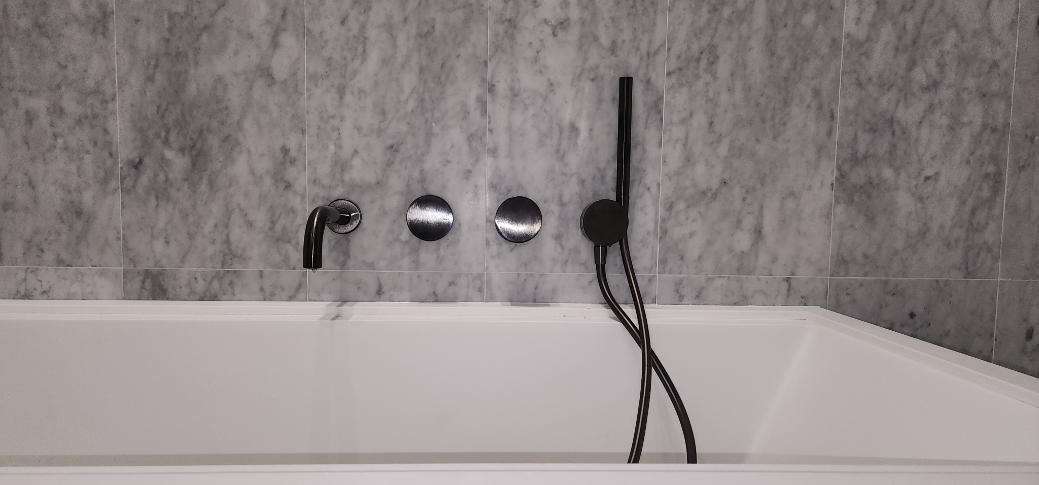 Biała wanna z czarną armaturą na tle marmurowych płytek w łazience. Minimalistyczny design, widoczne detale wykończenia.