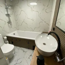 Nowoczesna łazienka z wanną obudowaną drewnianą okładziną, umywalką nablatową na drewnianym blacie i marmurowymi płytkami na ścianach i podłodze.