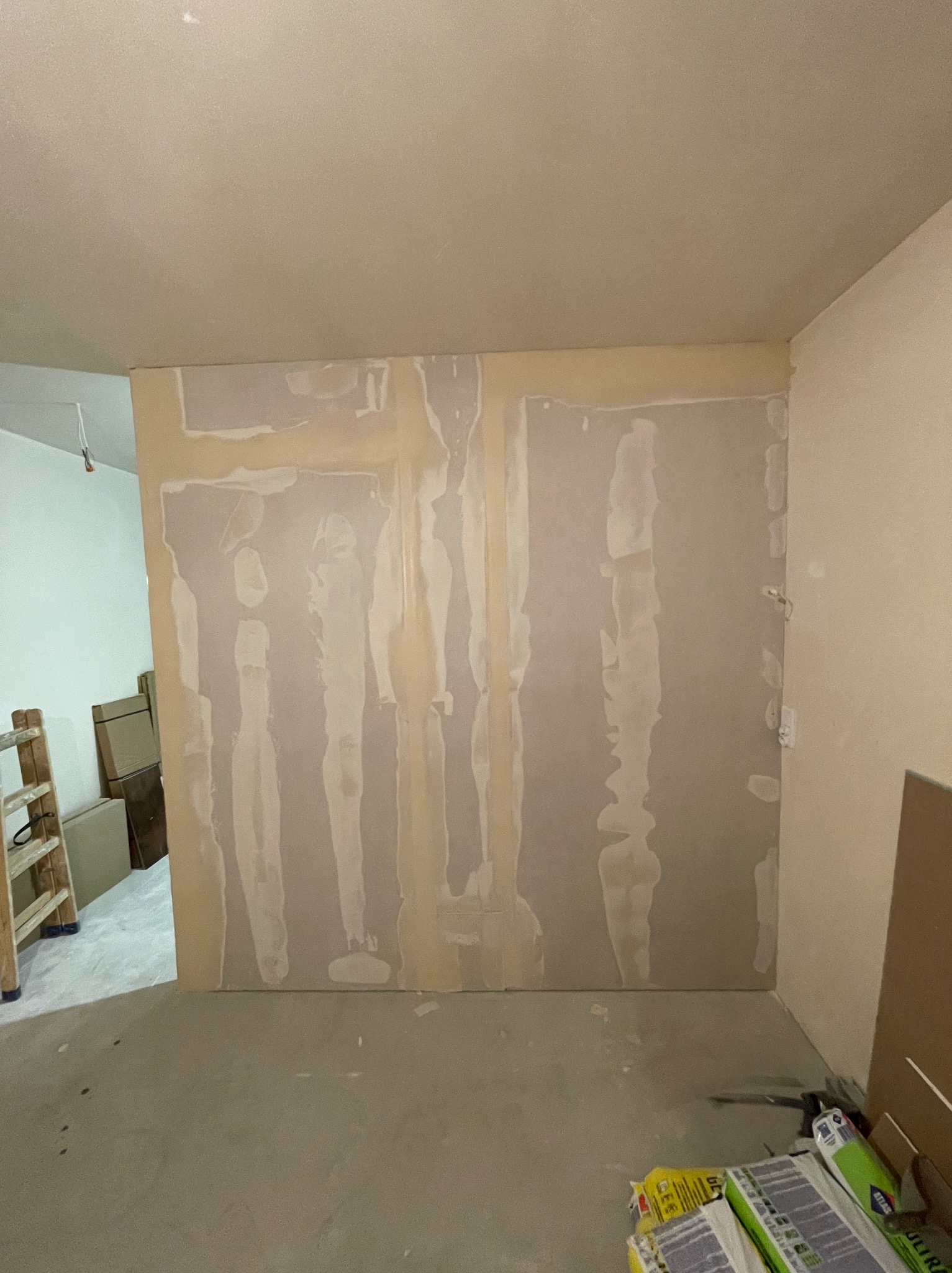 Wnętrze w trakcie prac wykończeniowych: ściana z płyt gipsowo-kartonowych z widocznymi łączeniami pokrytymi masą szpachlową, przygotowywana do dalszej obróbki.