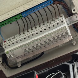 Emil Prochownik - Rozdzielnica elektryczna z zamontowanymi bezpiecznikami i podłączonymi przewodami w kolorach: brązowym, niebieskim, żółto-zielonym. Widoczne listwy zaciskowe.