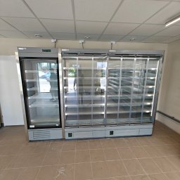Arbilem Daria Piechota - Nowoczesne, przeszklone chłodziarki w sklepie, z pustymi półkami, oświetlone LED, gotowe do ekspozycji produktów. Widok na wnętrze sklepu przez szyby.