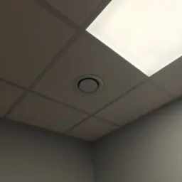 Kasetonowy sufit podwieszany z okrągłym nawiewnikiem wentylacyjnym i panelem oświetleniowym, widok z dołu pod kątem w szarym pomieszczeniu biurowym.