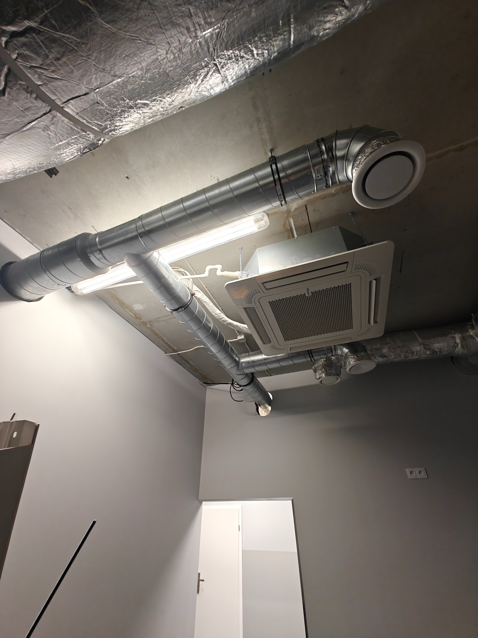 Instalacja wentylacji mechanicznej z rekuperacją w biurze w Częstochowie. Widoczne rury wentylacyjne, klimatyzator kasetonowy i oświetlenie.