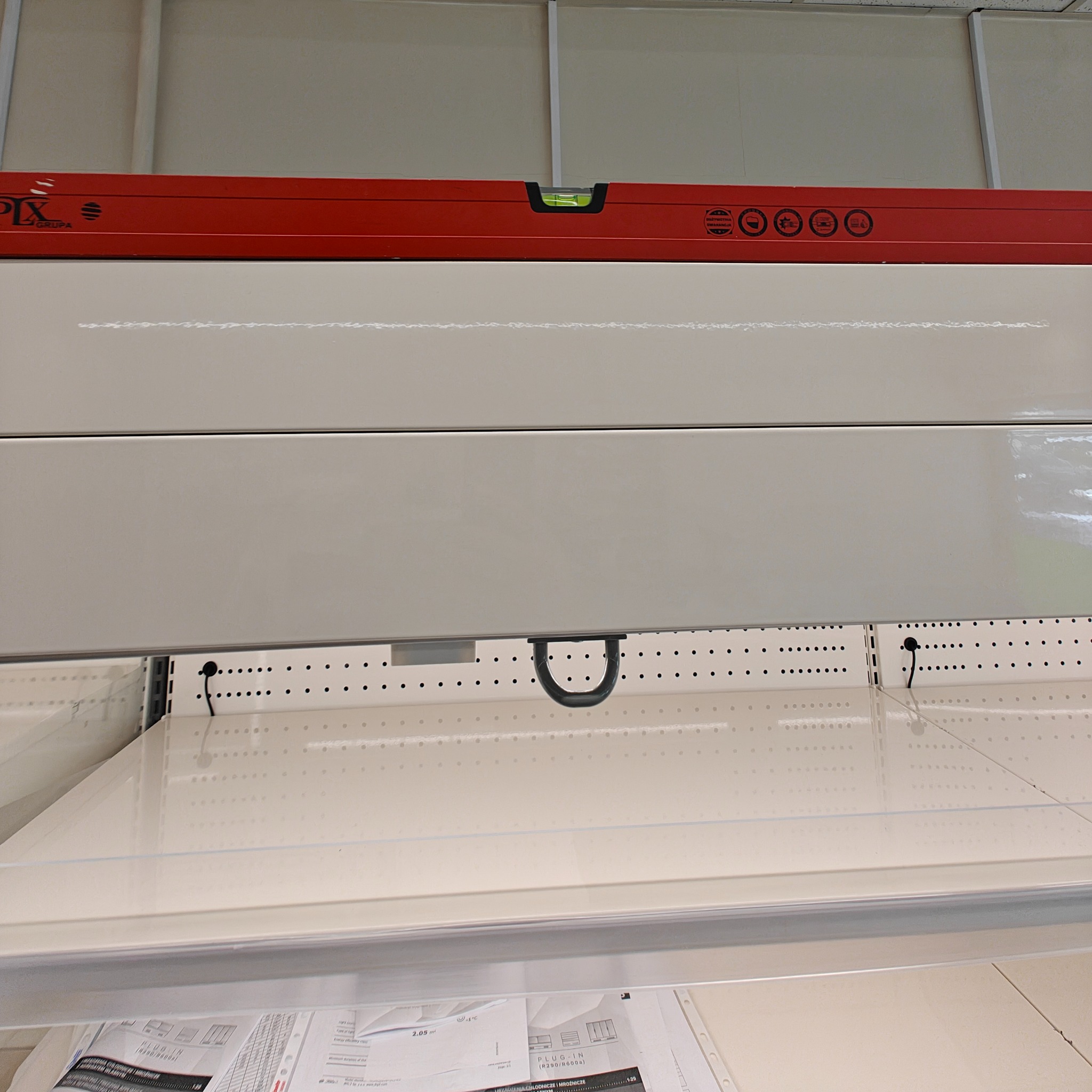Poziomica PIX Grupa na tle białych paneli i perforowanej ściany. Widoczne oznaczenia producenta i symbole. Dokumenty techniczne na dolnej półce.