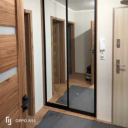 Szafa wnękowa z lustrzanymi drzwiami przesuwnymi w korytarzu mieszkania w Piławie G&oacute;rnej, widoczne drzwi do innych pomieszczeń i szary dywanik.