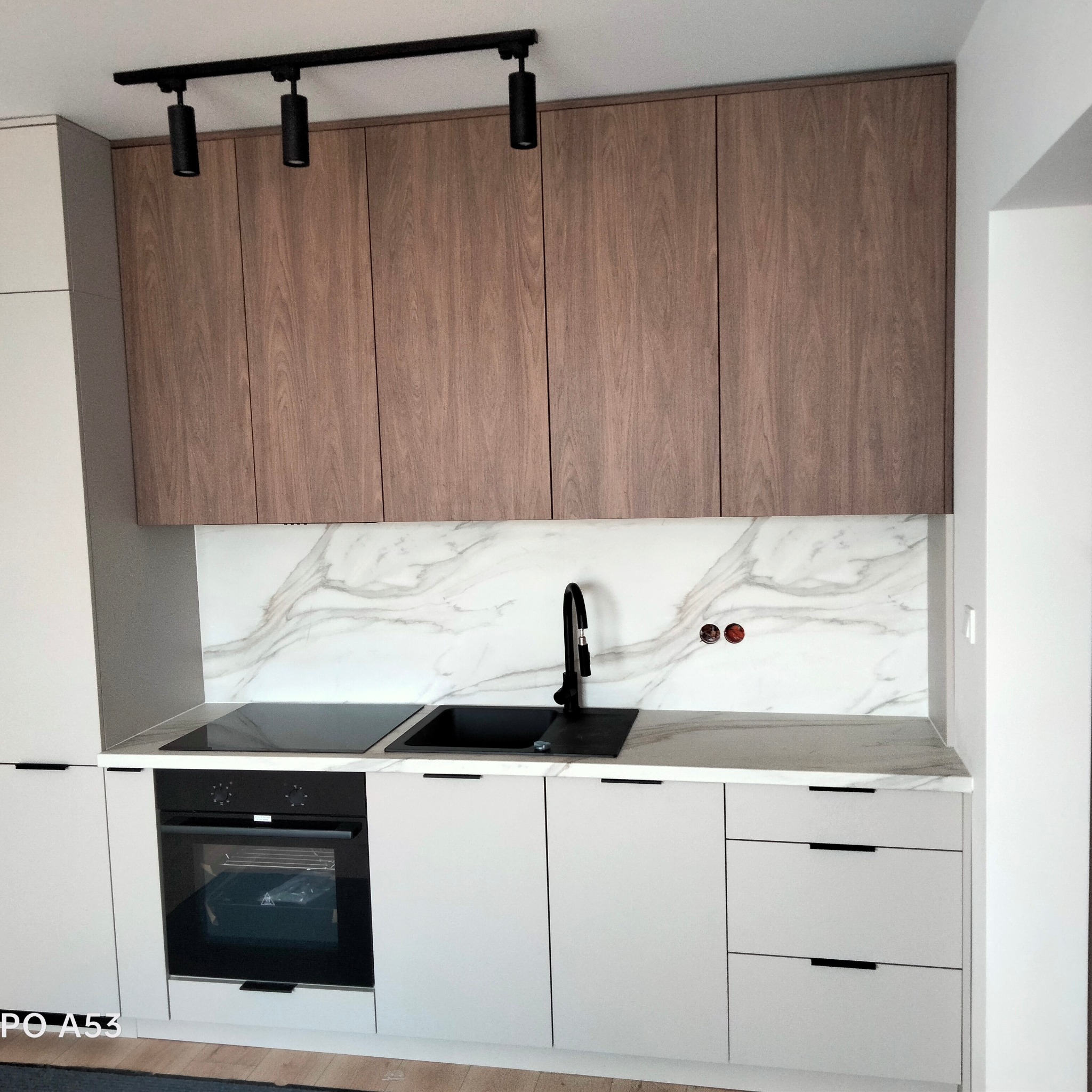 Nowoczesna kuchnia z drewnianymi szafkami górnymi, białymi szafkami dolnymi, czarną armaturą i blatem imitującym marmur.