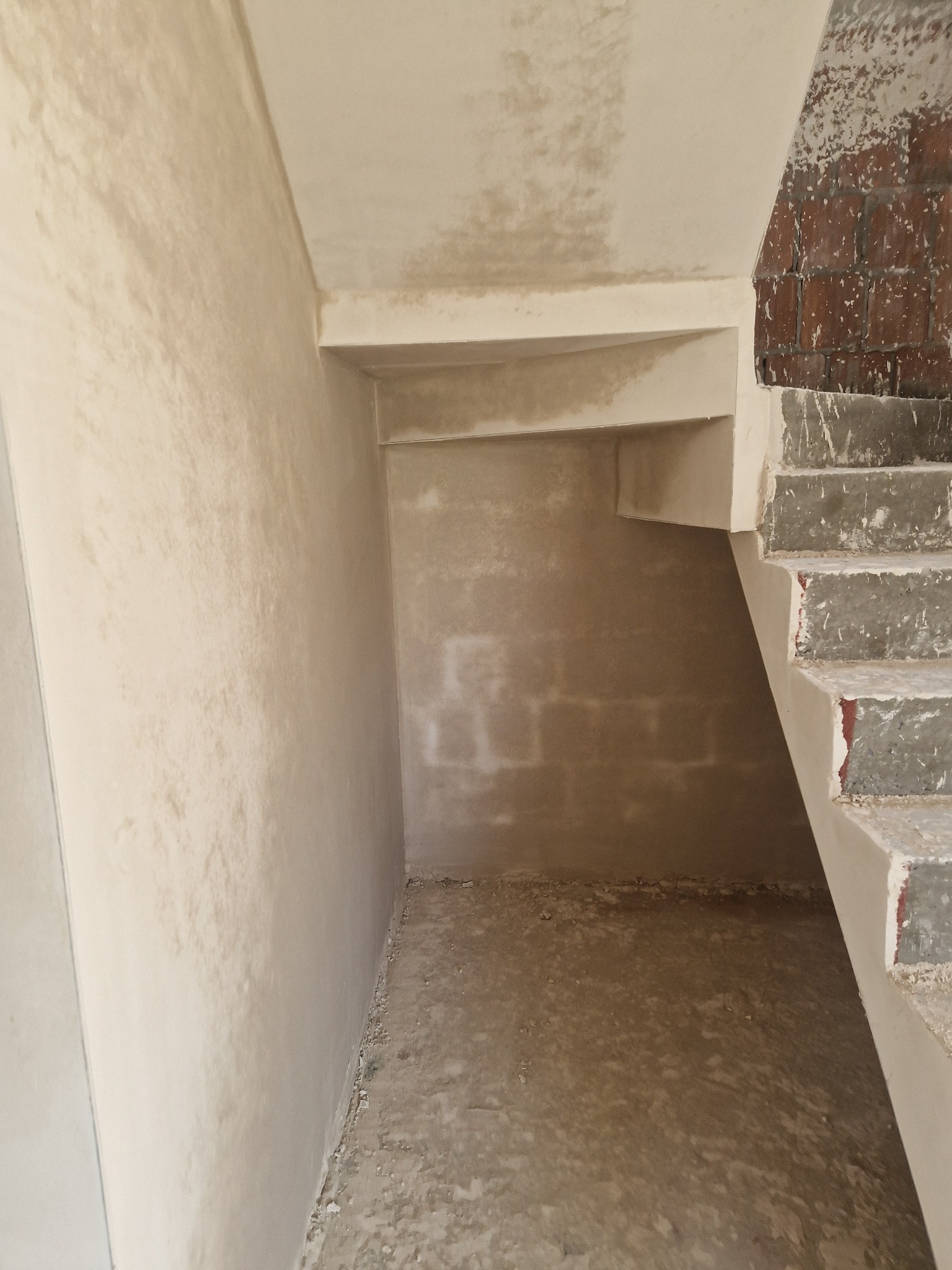 Świeżo położone, jasne tynki na ścianach i suficie w surowym wnętrzu klatki schodowej, widoczne fragmenty schodów z ceglanym wykończeniem.