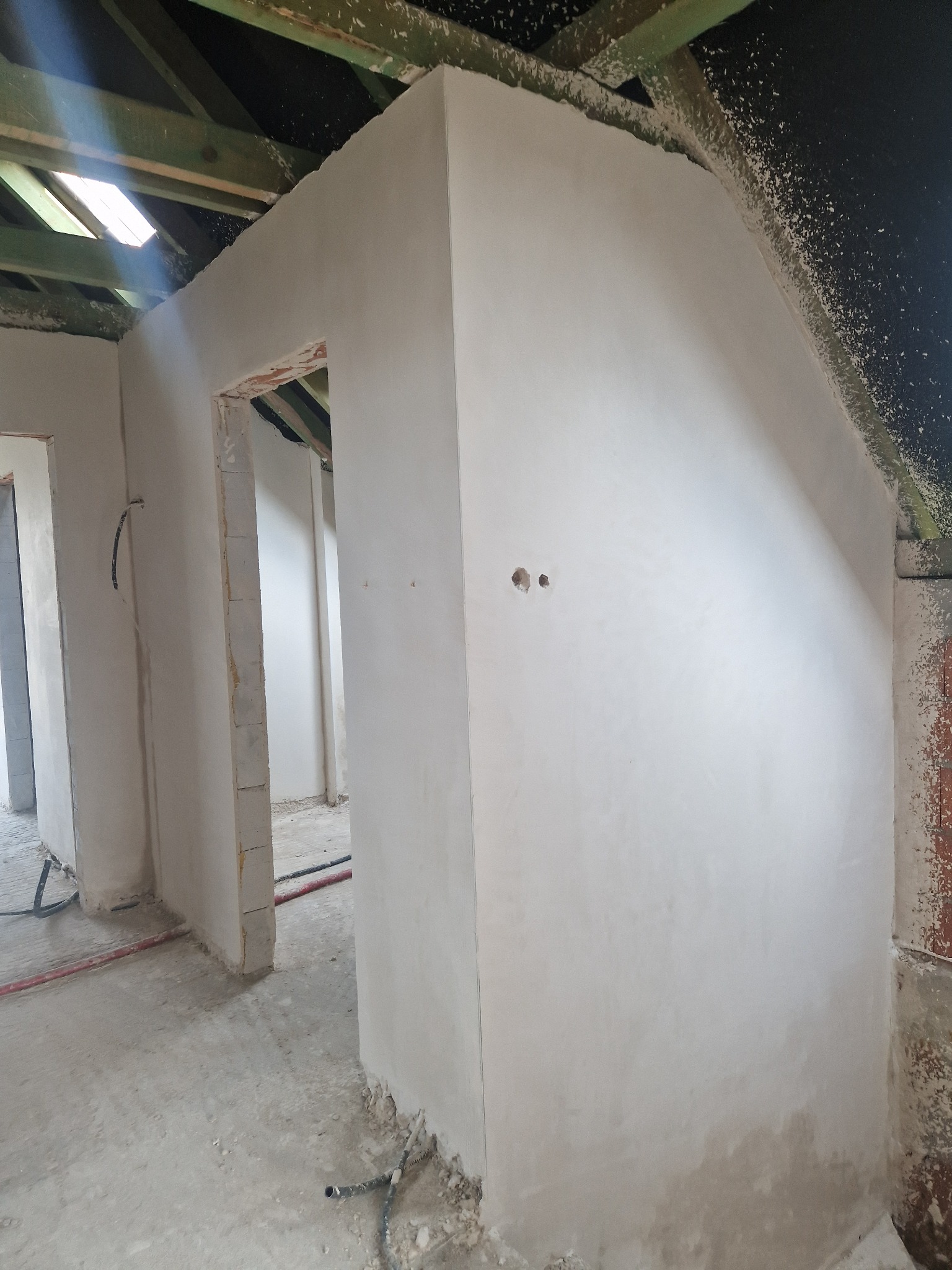 Świeżo położone, gładkie tynki na ścianach poddasza z widoczną drewnianą konstrukcją dachu i otworami na instalacje elektryczne.