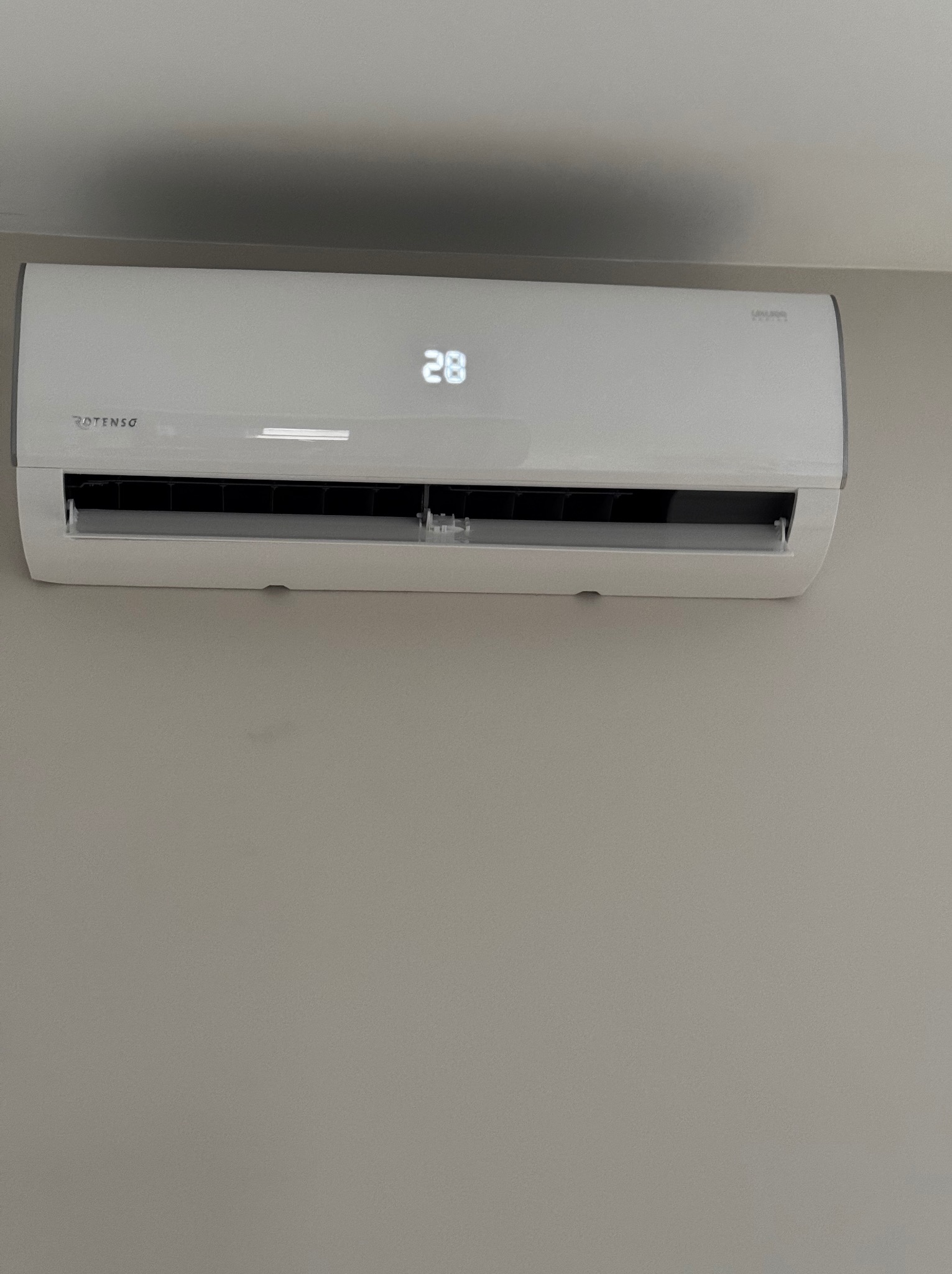 Biała klimatyzacja Rotenso zamontowana na ścianie, wyświetlająca temperaturę 28 stopni. Widoczne logo marki.