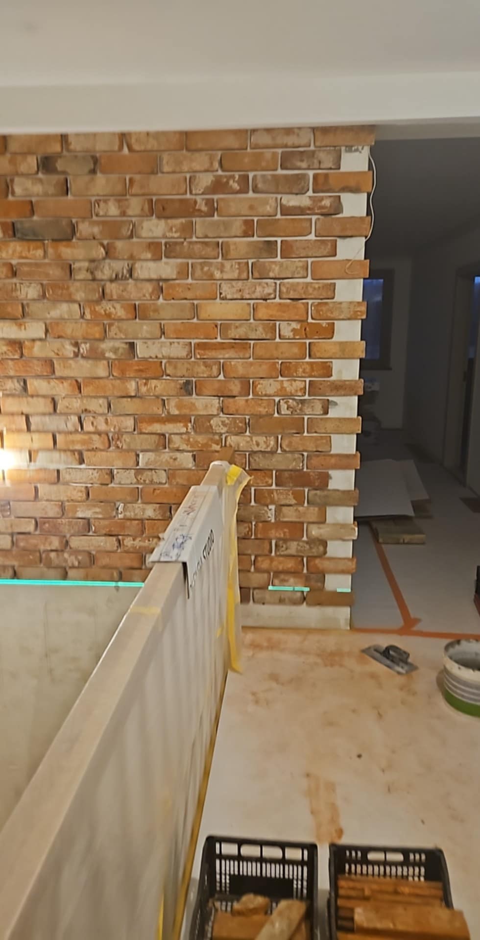 Wnętrze w trakcie wykańczania: ściana z cegły klinkierowej ułożona do pewnej wysokości, widoczny laserowy poziom, narzędzia i materiały budowlane.