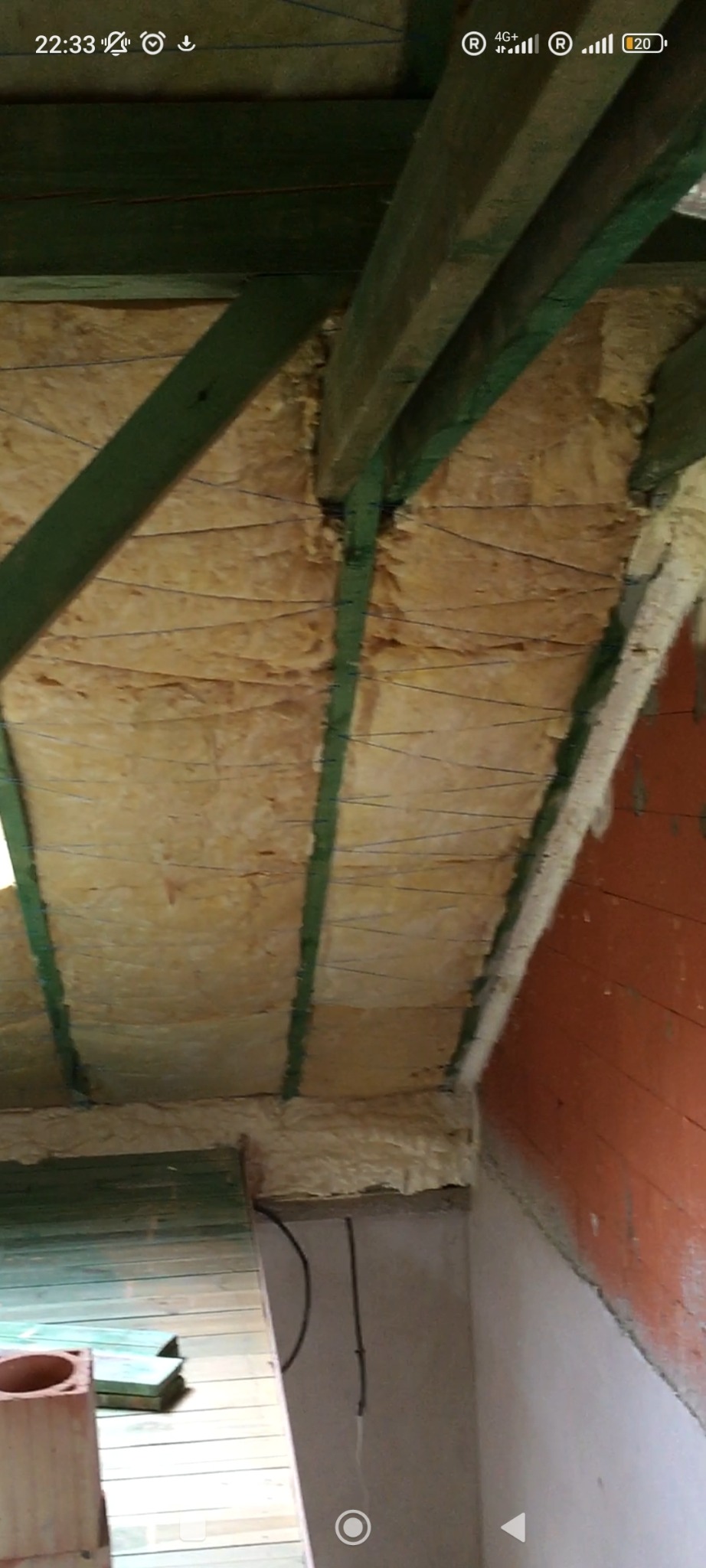 Izolacja poddasza z widoczną wełną mineralną przymocowaną sznurkami do drewnianej konstrukcji dachu. Widoczne fragmenty ścian i podłogi.