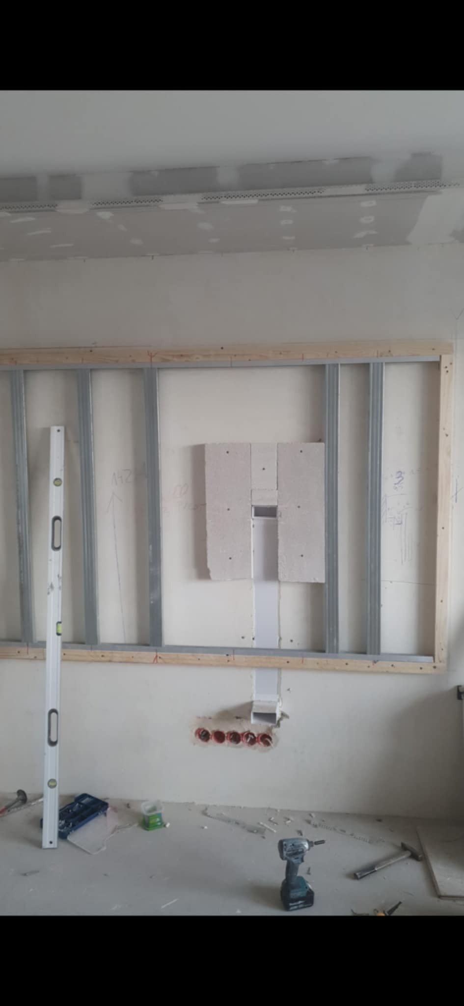 Stelaż pod zabudowę ściany z płyt gipsowo-kartonowych, widoczne przewody elektryczne i poziomica przy metalowym profilu. Etap prac wykończeniowych.