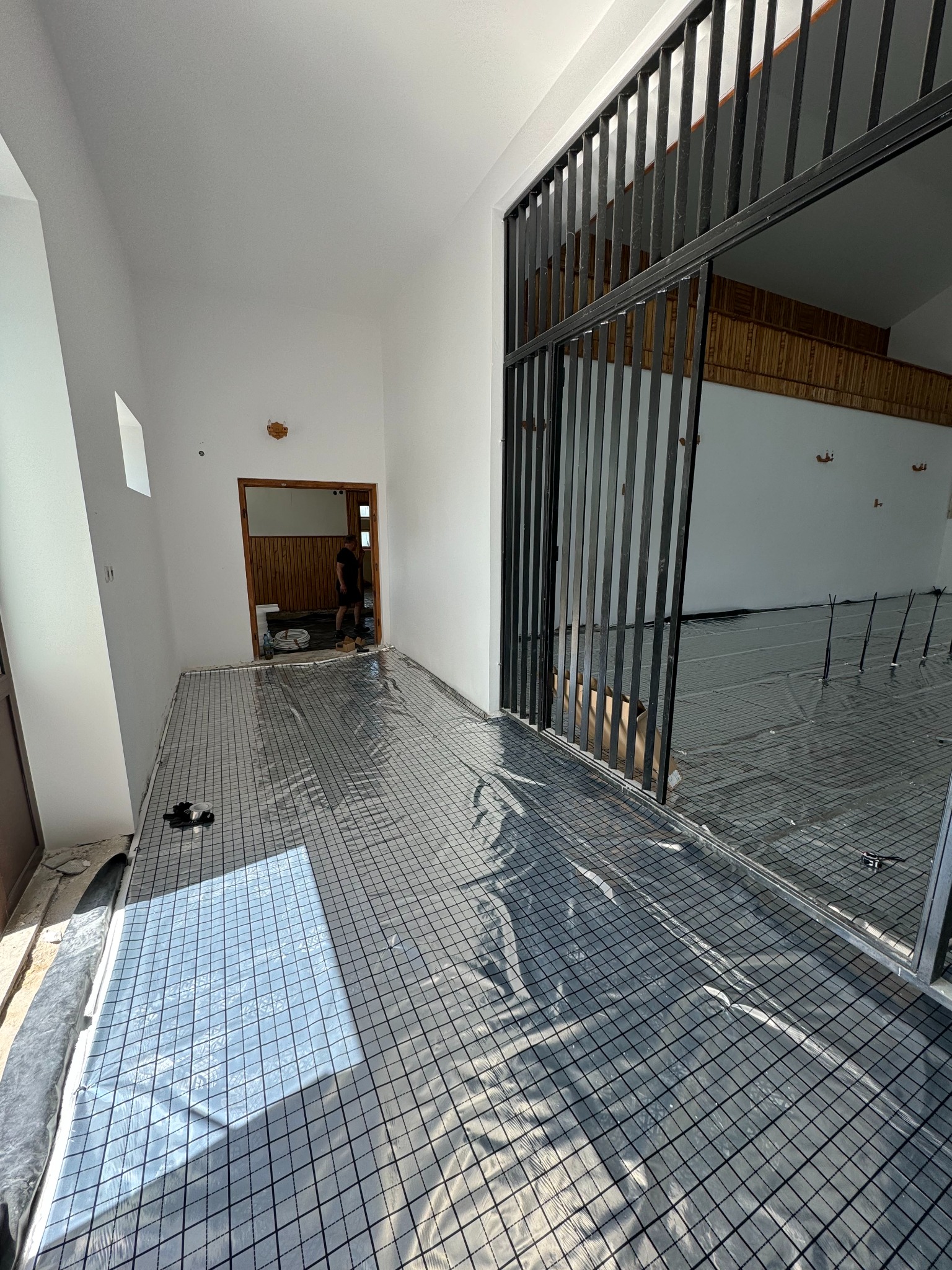 Rozłożona siatka z folią na podłodze, przygotowana do montażu ogrzewania podłogowego w jasnym pomieszczeniu z widoczną konstrukcją metalową.