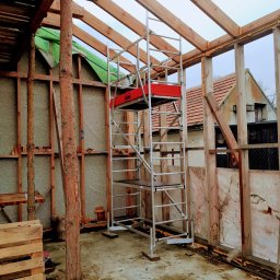 Eagle Tech Krystian Orłowski - Wnętrze w trakcie budowy: drewniana konstrukcja szkieletowa z izolacją, rusztowanie na środku, widoczne elementy mocowań i pianka uszczelniająca.