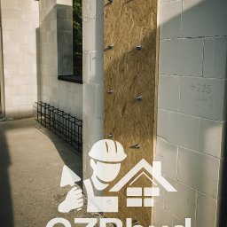 GZB - Kompleksowe prace ziemne, murarskie - Ściana z betonu komórkowego w trakcie budowy, wzmocniona płytą OSB, widoczne zbrojenia. Częściowo oświetlona promieniami słonecznymi.