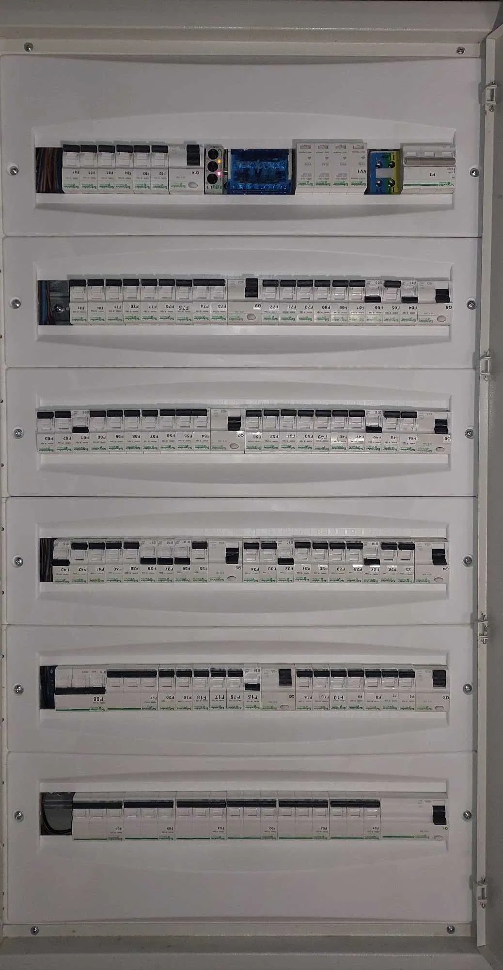 Rozdzielnia elektryczna z wieloma bezpiecznikami, widok z bliska, biała obudowa, czarne przełączniki, oznaczenia na bezpiecznikach, przewody w górnej części.