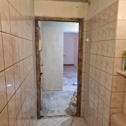 Mazur.s.m - Łazienka w trakcie remontu: stare, beżowe płytki na ścianach i podłodze, widoczny surowy stan ściany nad drzwiami, niedomalowany sufit i toaleta w stylu retro.