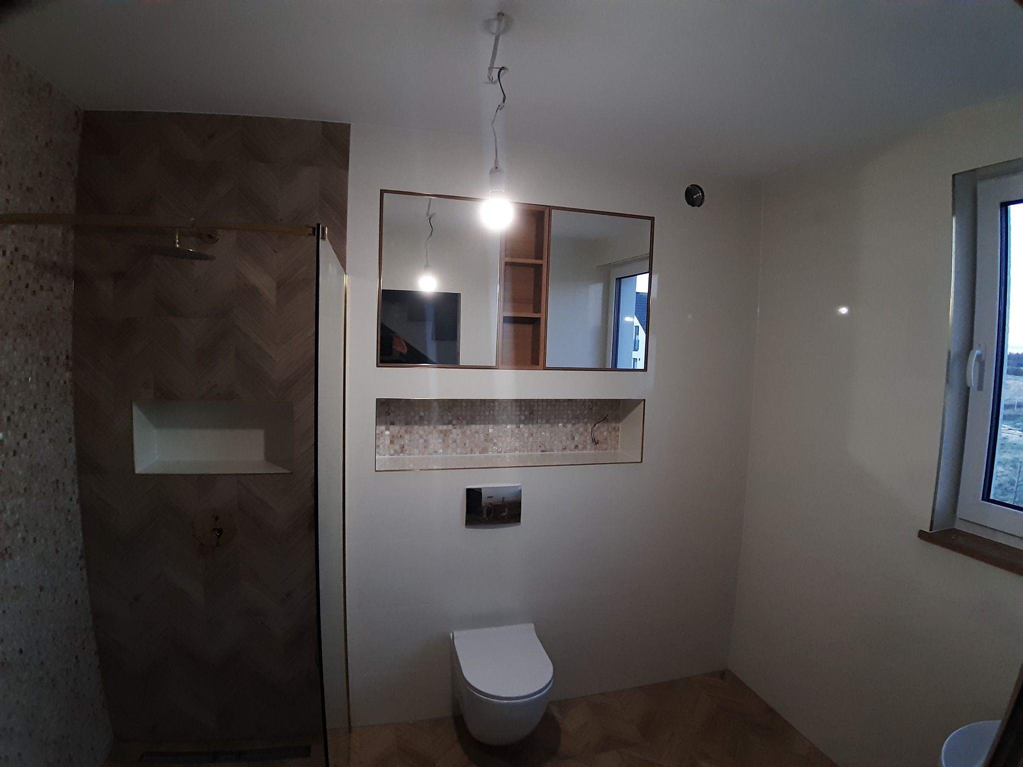 Wykończona łazienka w Bolszewie: kabina prysznicowa z wzorem jodełki, podwieszana toaleta, lustro z półkami, okno z widokiem na zewnątrz. Nowoczesny design.