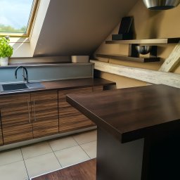 Luca Design - Kuchnia na poddaszu ze skośnym oknem dachowym, ciemnymi drewnianymi frontami szafek i blatem. Minimalistyczne półki i dekoracje. Jasna podłoga z płytek.