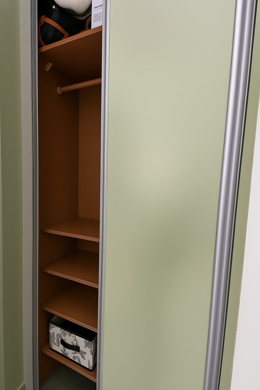 Otwarta szafa wnękowa z przesuwnymi drzwiami w odcieniach beżu i szarości. Widoczne półki i drążek na ubrania. Na półkach widoczne przedmioty.