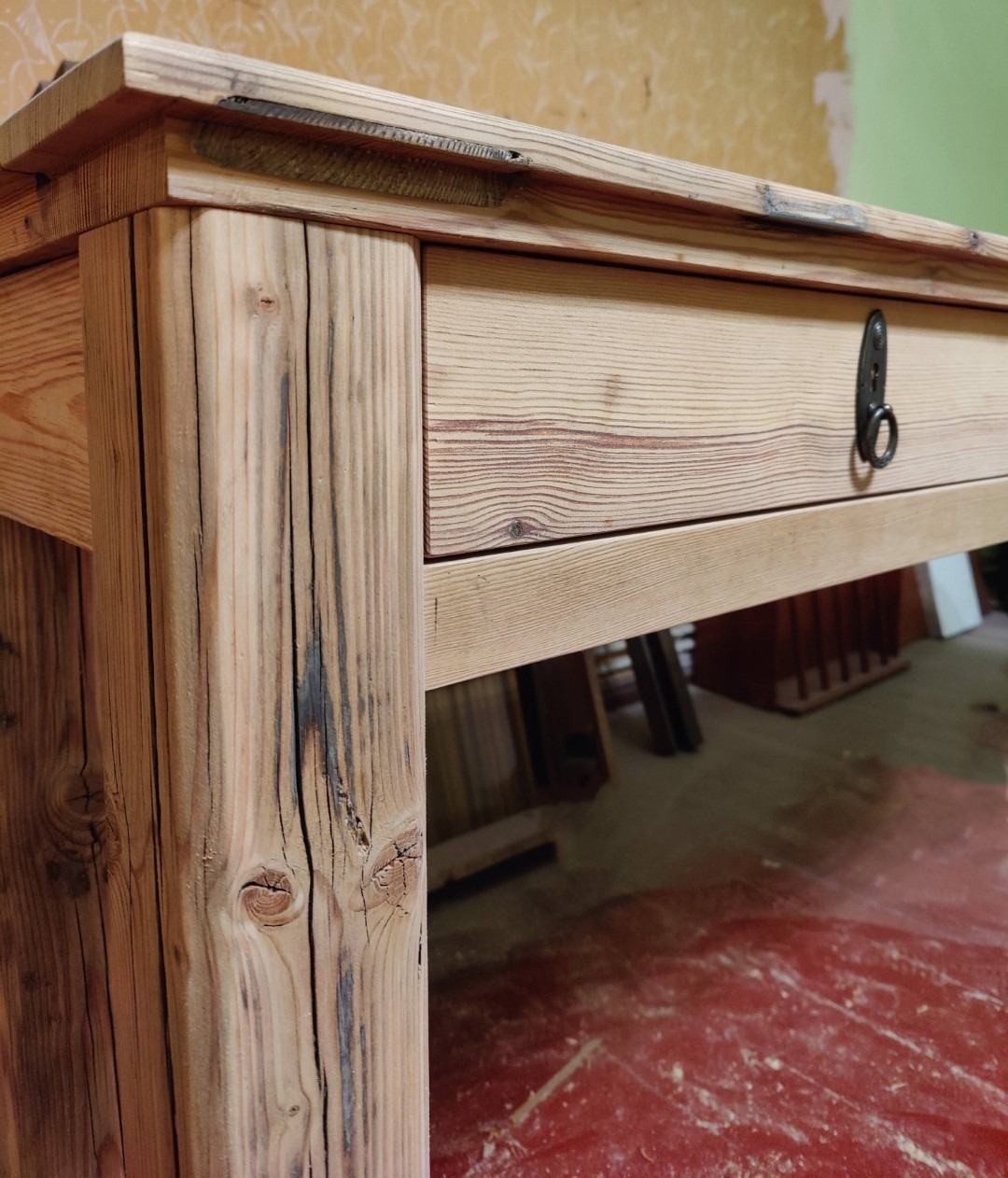 Stół z szufladą wykonany z jasnego drewna z widocznymi słojami i czarnymi śladami po opalaniu, metalowy uchwyt szuflady w kształcie łezki.