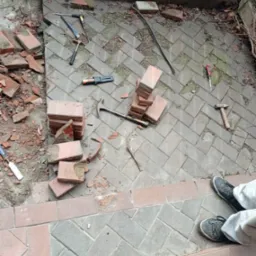 Uszkodzona kostka brukowa z narzędziami do naprawy: młotek, dłuto, śrubokręt i łom, częściowo zdemontowana, przygotowana do wymiany.