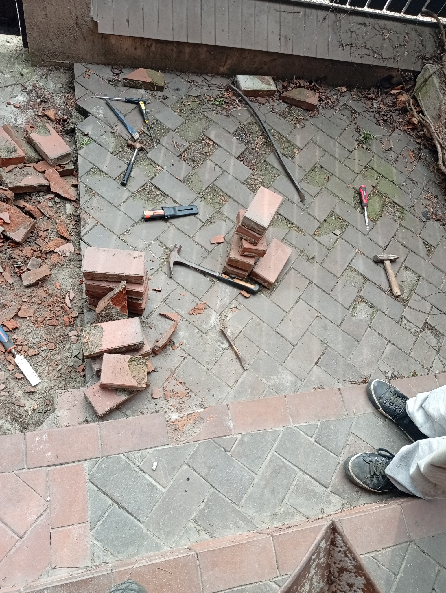 Uszkodzona kostka brukowa z narzędziami do naprawy: młotek, dłuto, śrubokręt i łom, częściowo zdemontowana, przygotowana do wymiany.