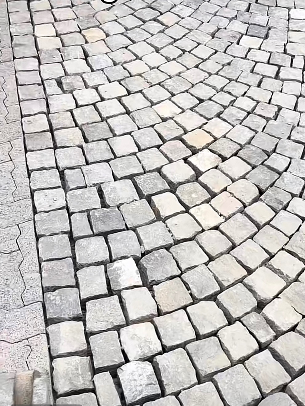 Szara kostka granitowa ułożona w łukowaty wzór, widoczna z bliska pod kątem. Krawędź wykończona inną, jaśniejszą kostką o regularnym kształcie.