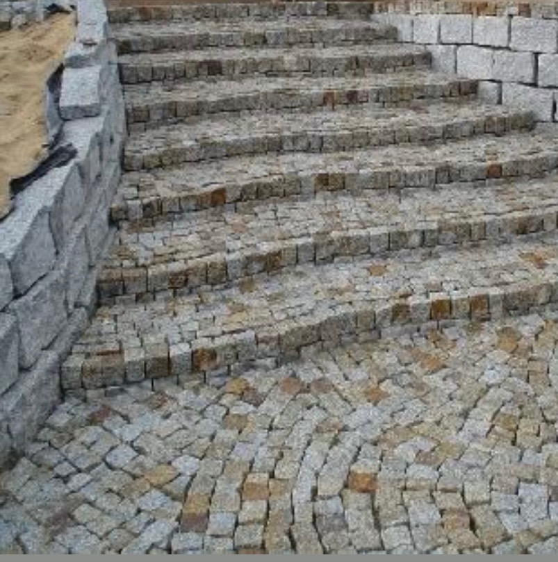 Granitowe schody zewnętrzne z kostki, łagodny łuk stopni, szara kolorystyka, solidne kamienne obrzeża, drobna faktura kostki, ukończony projekt.