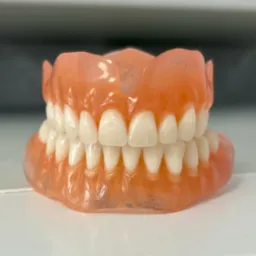 Kompletna proteza zębową na białym tle, widoczne detale różowego akrylu i białych zębów.