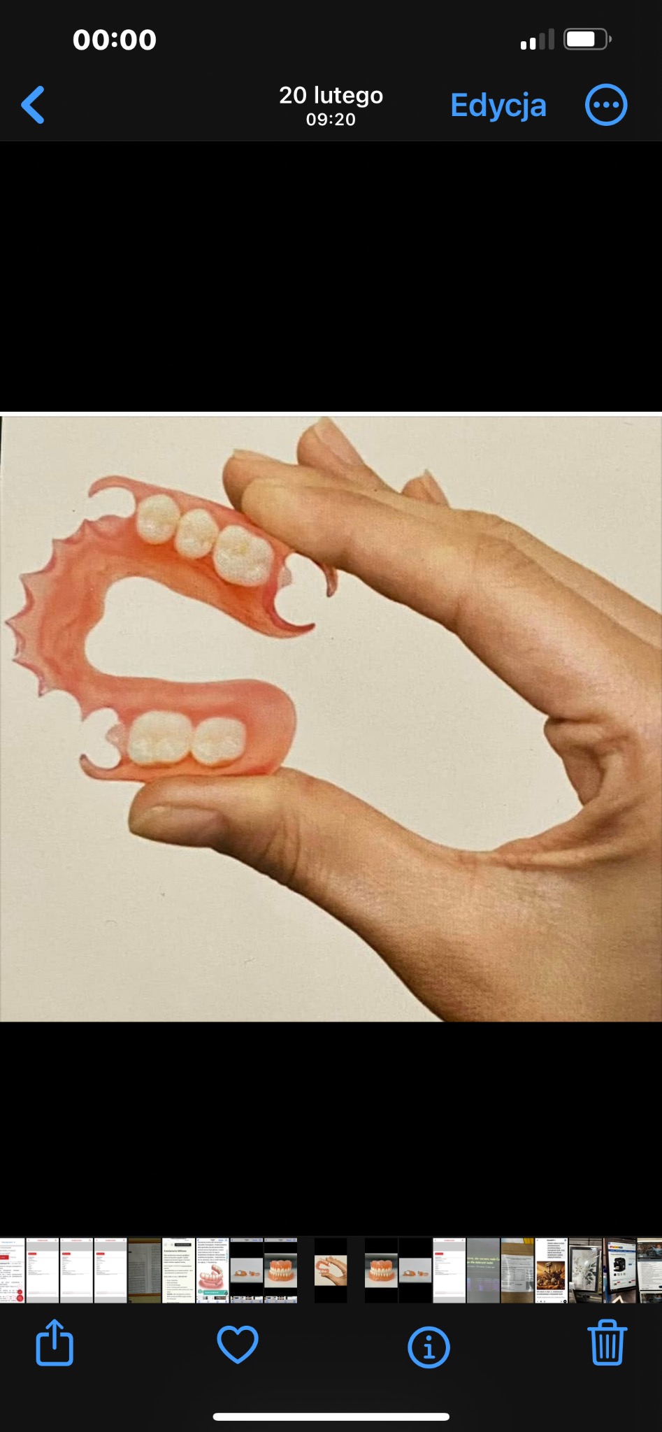 Elastyczna proteza częściowa górna, utrzymywana w palcach, z widocznymi białymi sztucznymi zębami i różowym akrylem, prezentowana na jasnym tle.