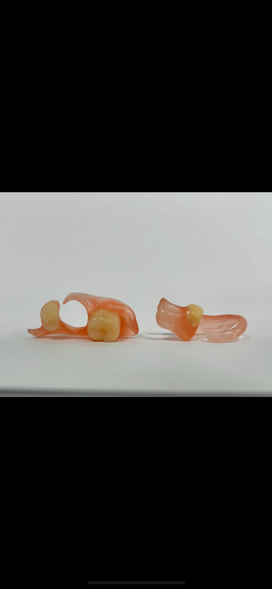 Dwie wyjmowane protezy częściowe z akrylu w odcieniach różu i beżu, leżące na białym tle.