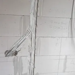 Białe kable elektryczne ułożone w bruzdach ściany z betonu komórkowego, z widocznymi oznaczeniami i notatkami na ścianie. Etap prac instalacyjnych.