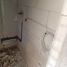 Artur Radecki - Wnętrze w trakcie prac: przewody elektryczne i rury wodne w ścianie z betonu komórkowego. Widoczne gruz i niedokończone wykończenie.