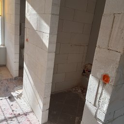 Artur Radecki - Wnętrze w trakcie budowy z widocznymi instalacjami elektrycznymi w ścianach z betonu komórkowego. Pomarańczowa puszka elektryczna i przewody w korytkach.