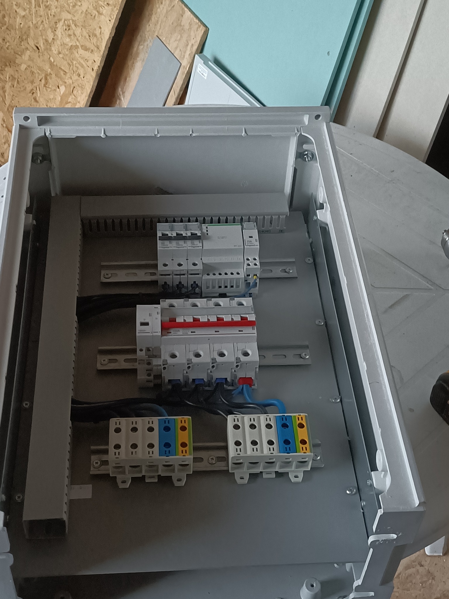 Otwarta, szara skrzynka rozdzielcza z zamontowanymi bezpiecznikami, listwami zaciskowymi i przewodami. Widok z góry, wnętrze skrzynki oświetlone.