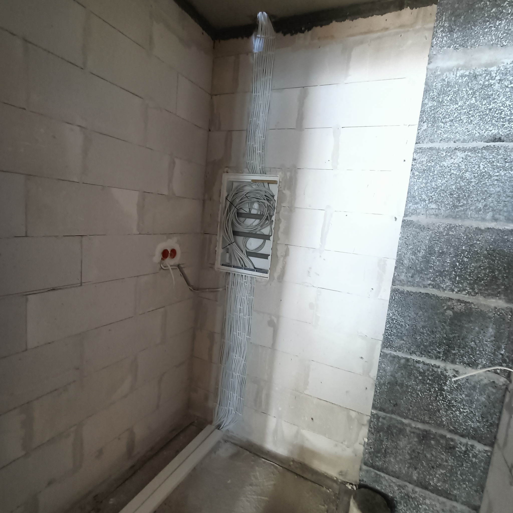 Surowy stan: białe kable w listwach prowadzone pionowo po ścianie z betonu komórkowego, w tle szara ściana z pustaków. Widoczna puszka instalacyjna z kablami.