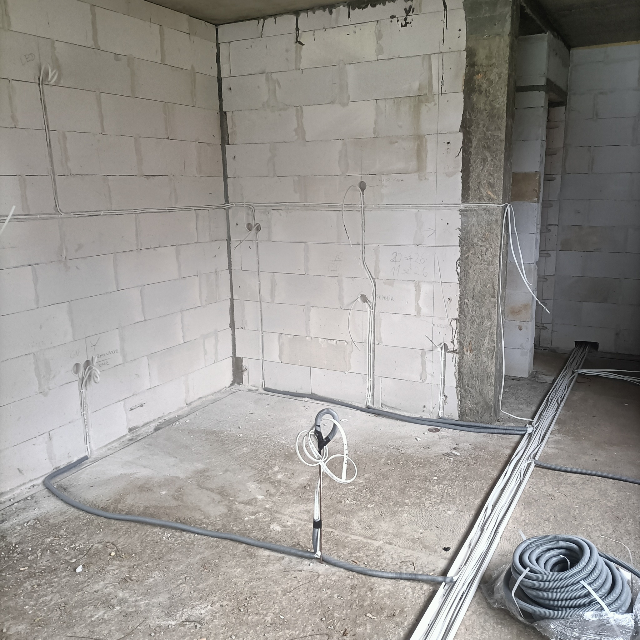 Wnętrze w trakcie prac elektrycznych: kable w peszlach ułożone wzdłuż ścian z betonu komórkowego, widoczne punkty wyprowadzenia przewodów.