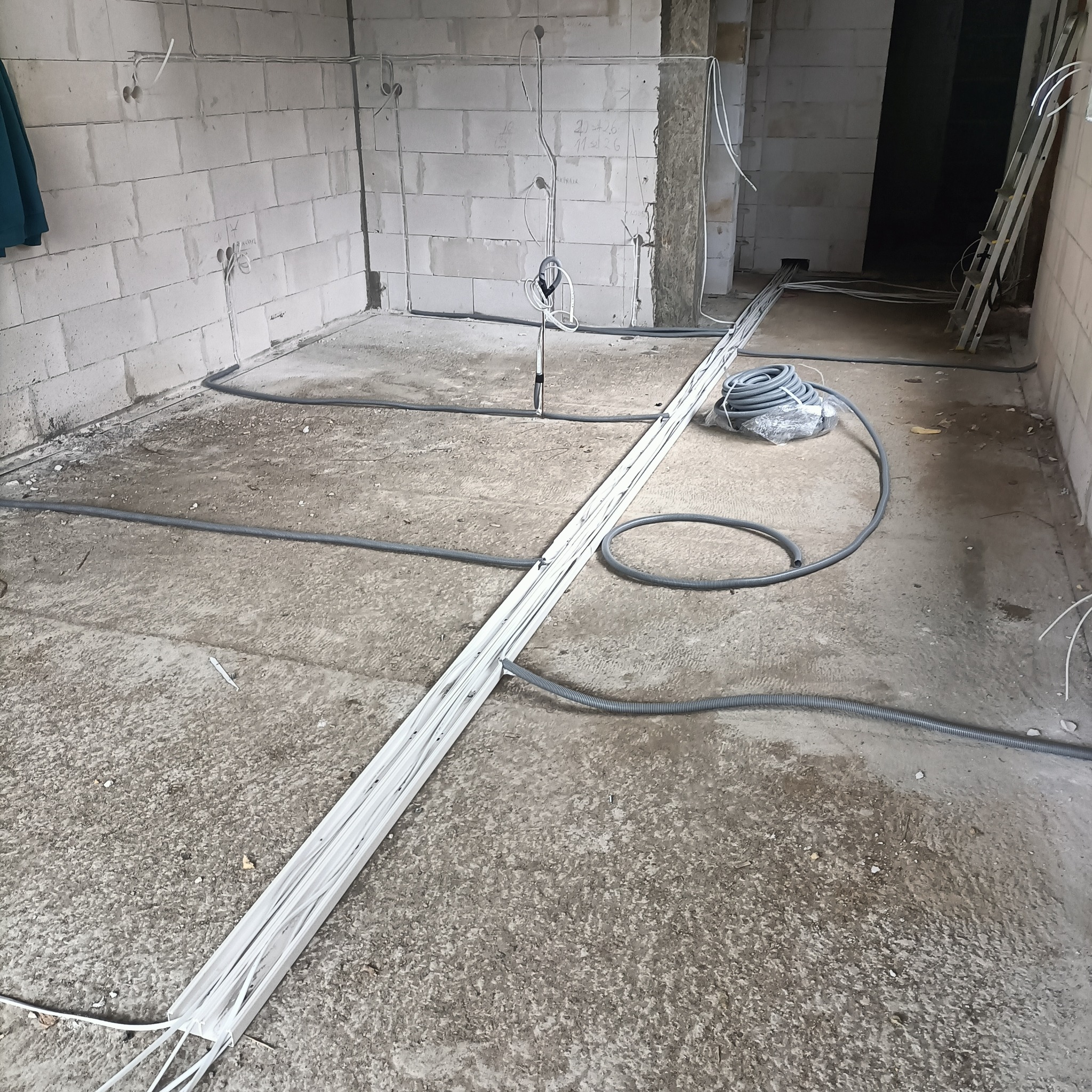 Surowy stan instalacji elektrycznej w Szczecinku: kable prowadzone po podłodze w szarych rurach, puszki na ścianach z białego bloczka.