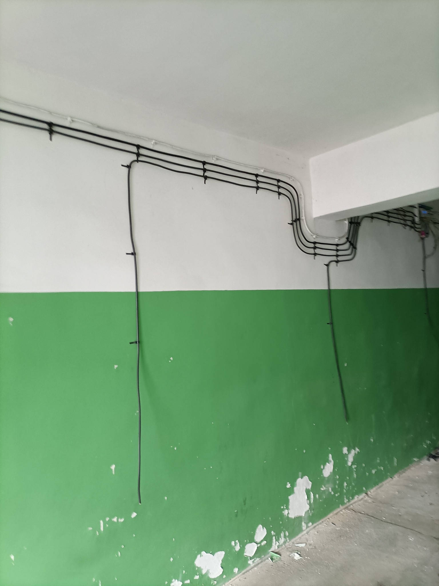 Ściana z instalacją elektryczną: czarne kable przymocowane do ściany pomalowanej na biało i zielono, widoczne mocowania kabli.