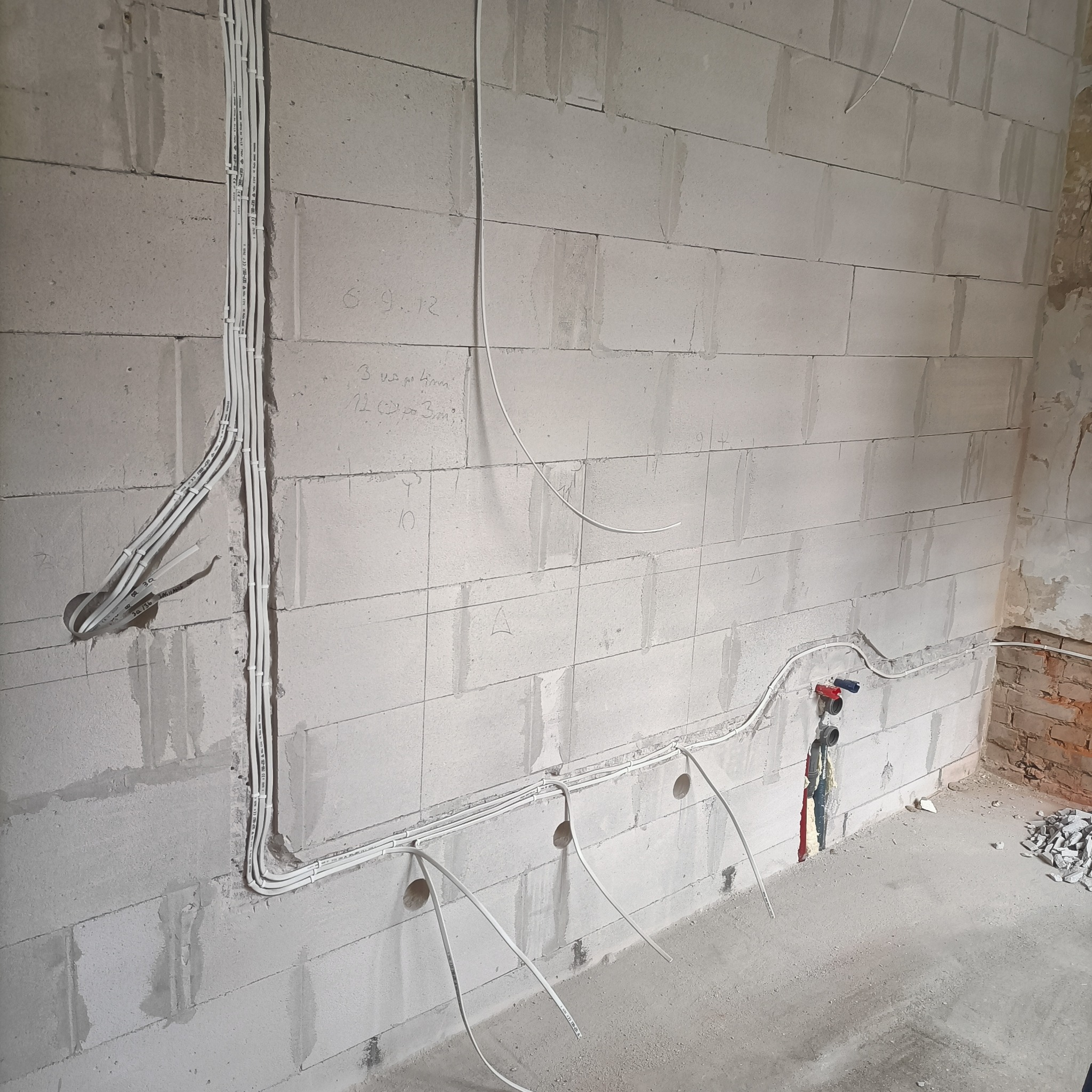 Instalacja elektryczna w ścianie z betonu komórkowego, widoczne kable prowadzone w peszlach i puszki instalacyjne. Ściana zarysowana, przygotowana do tynkowania.