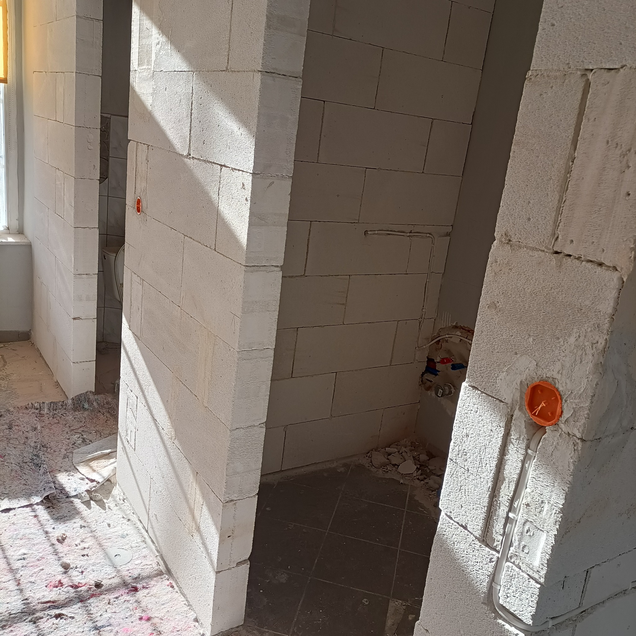 Wnętrze w trakcie budowy z widocznymi instalacjami elektrycznymi w ścianach z betonu komórkowego. Pomarańczowa puszka elektryczna i przewody w korytkach.