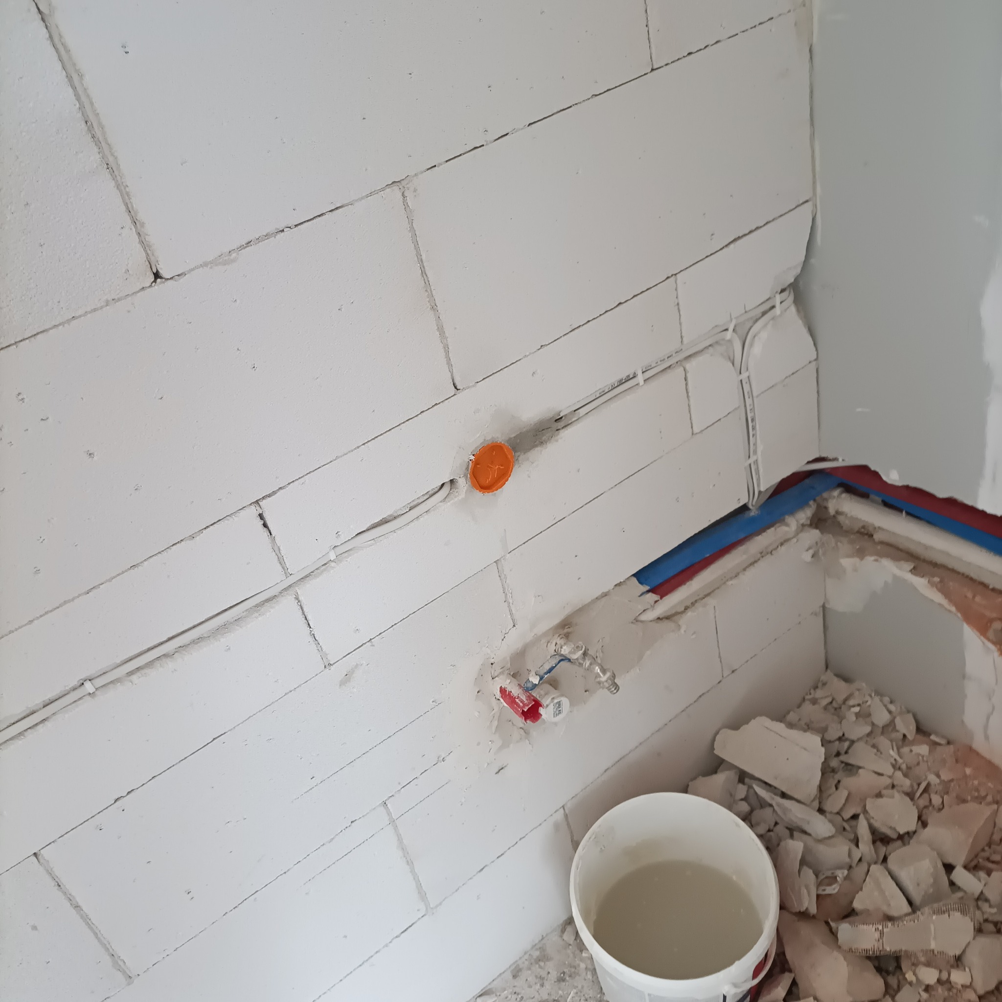 Białe ściany z betonu komórkowego w trakcie prac instalacyjnych: widoczne przewody elektryczne w peszlach, puszka instalacyjna i fragment instalacji wodnej.