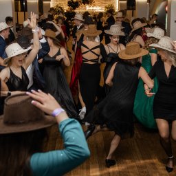 PHOTOLA Aleksandra Krzan - Rozbawieni goście w kowbojskich kapeluszach tańczą w sali balowej podczas studniówki, widoczny napis 'Studniówka' w tle.